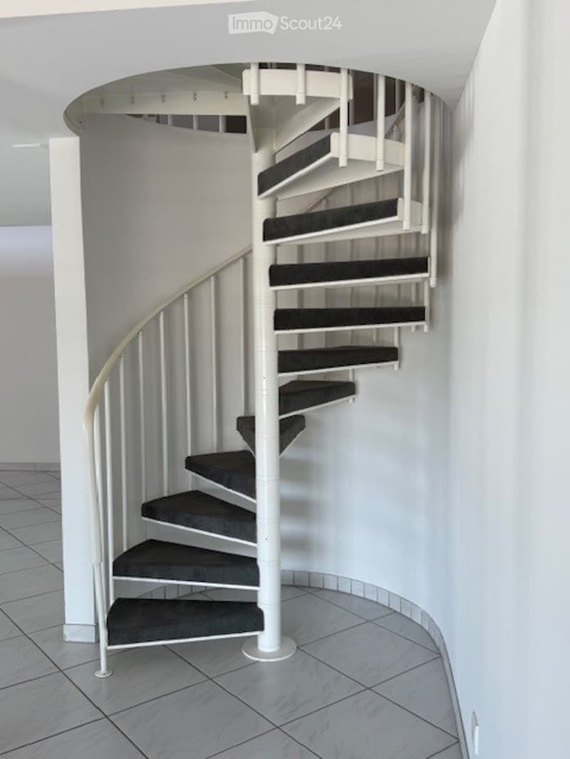Spiral staircase with white railings and dark grey steps, set in a modern interior with tiled flooring and white walls.