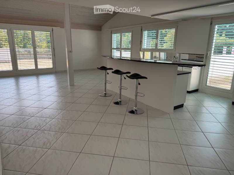 Open-plan kitchen and living area with tiled flooring, large windows, and a kitchen island with bar stools.