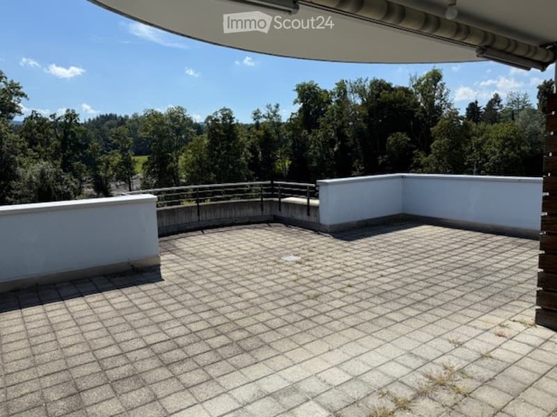 Spacious balcony with tiled floor, white walls, metal railing, and scenic view of trees and hills.
