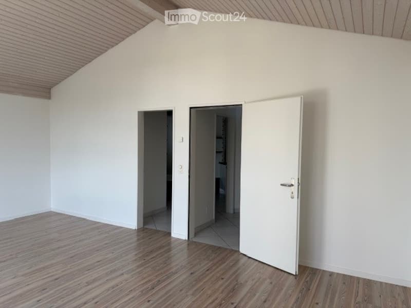 Empty room with wooden flooring, white walls, and multiple doors leading to other spaces.