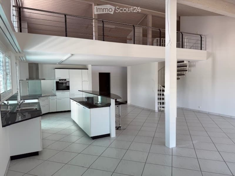 Modern, open-concept kitchen with white cabinetry, black countertops, and a central island. Features include a sink, faucet, oven, refrigerator, and a single stool near the island.