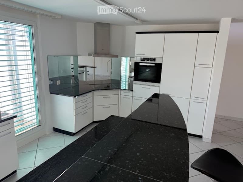 Modern kitchen with white cabinets, black countertops, and built-in oven. Features a large island with a black countertop and a single black stool.