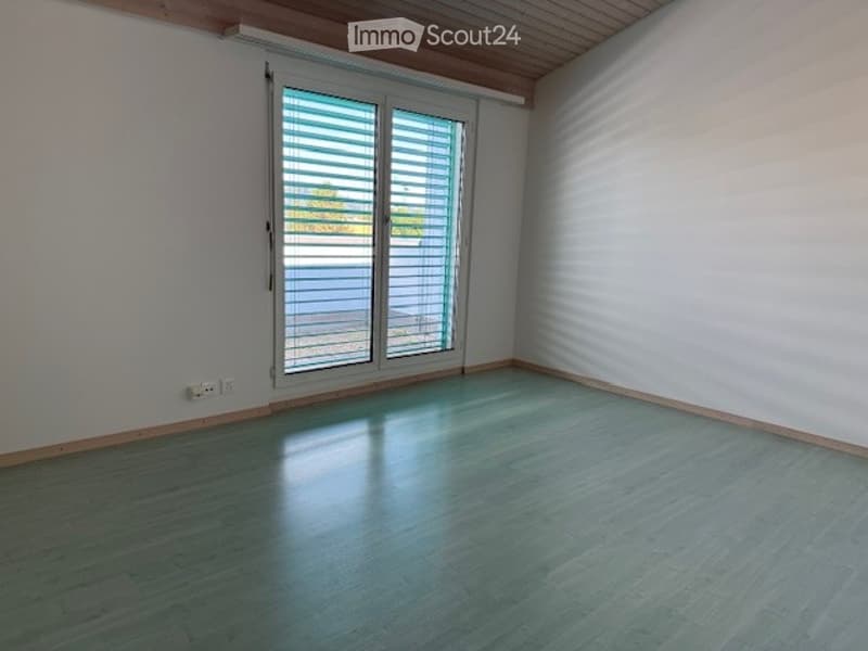 Empty room with wooden flooring, white walls, and large sliding glass doors with blinds.
