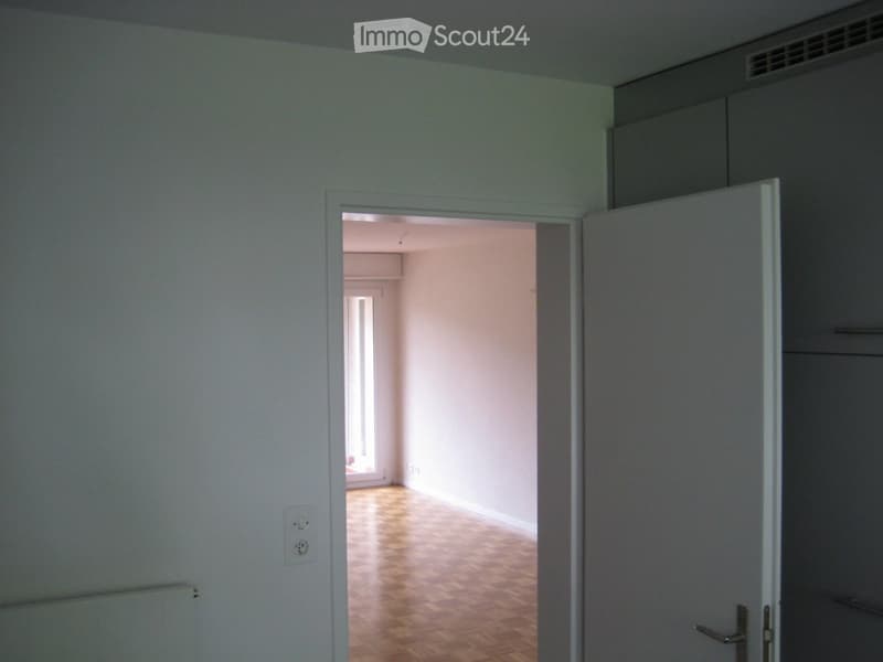 Empty room with light-colored walls, wooden flooring, and a partially open door leading to another room.