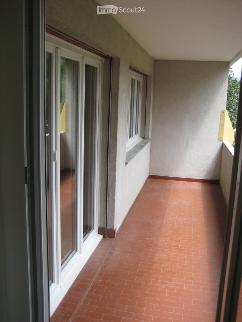 Balcony with red tiled floor, white walls, and large windows with sliding glass doors.