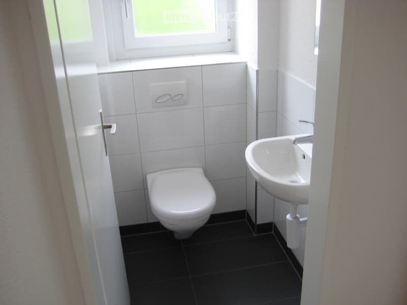 Modern bathroom with white tiles, black floor, toilet, sink, and window.