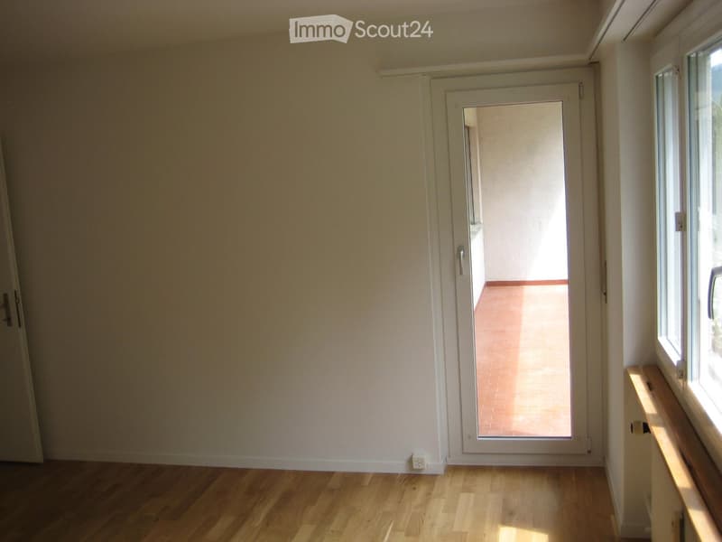 Empty room with wooden flooring, white walls, and a sliding glass door leading to a balcony.