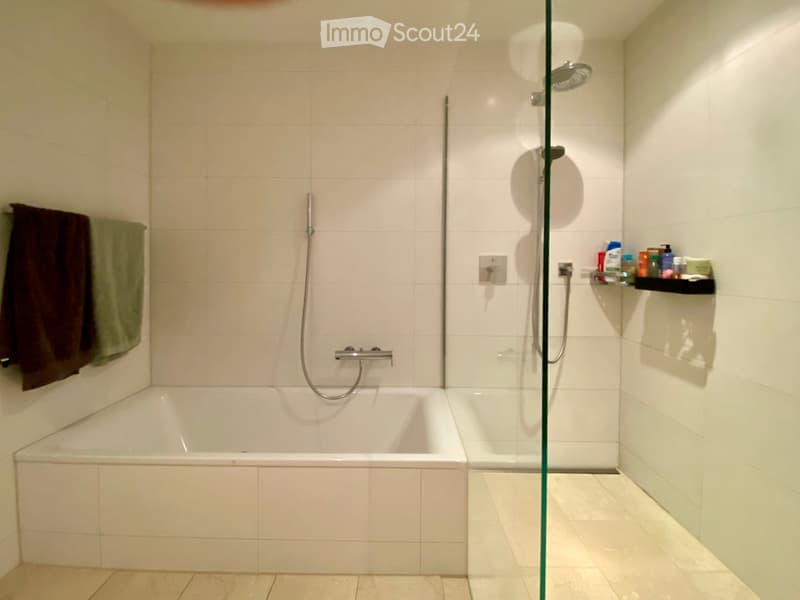 Modern bathroom with a bathtub, glass-enclosed shower, tiled walls, and a shelf with toiletries.