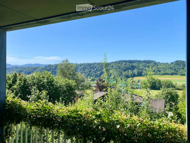 Balcony with a view of a lush green landscape, trees, and distant hills under a clear blue sky.