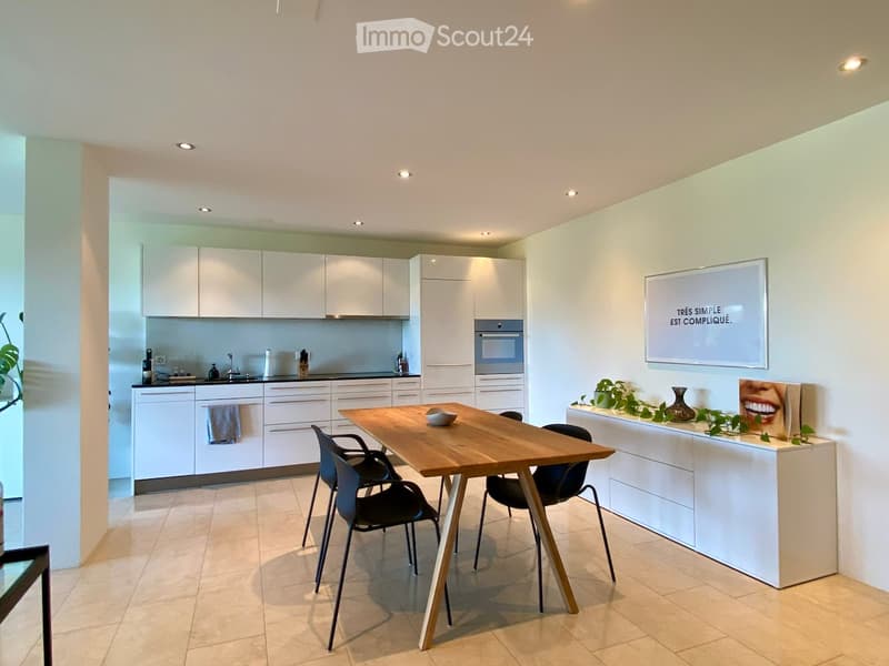 Modern kitchen with white cabinets, a wooden dining table, black chairs, and a small island with a vase and plants.