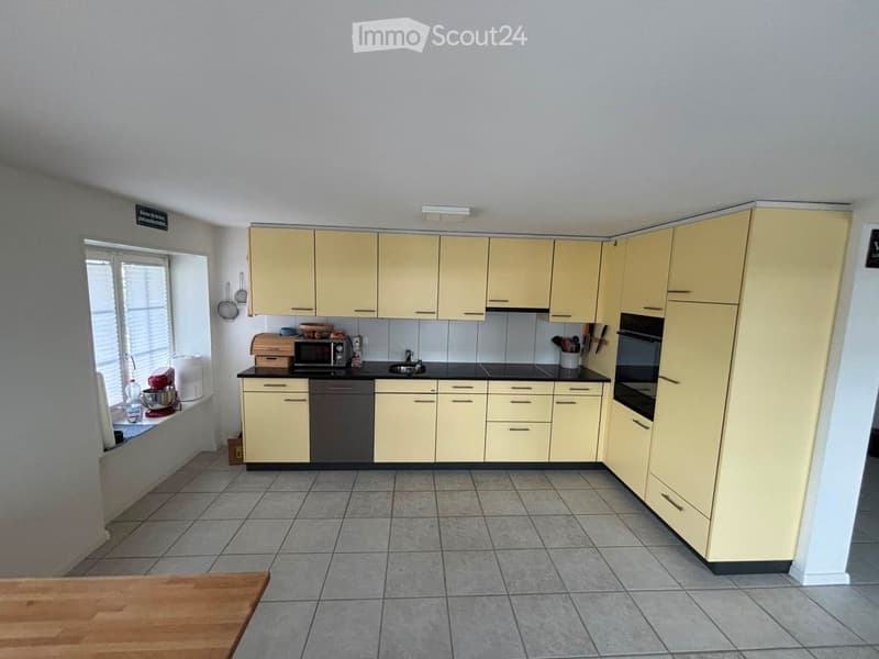 Bright kitchen with light yellow cabinets, black countertops, and tiled flooring. Includes a sink, microwave, oven, and various kitchen appliances.