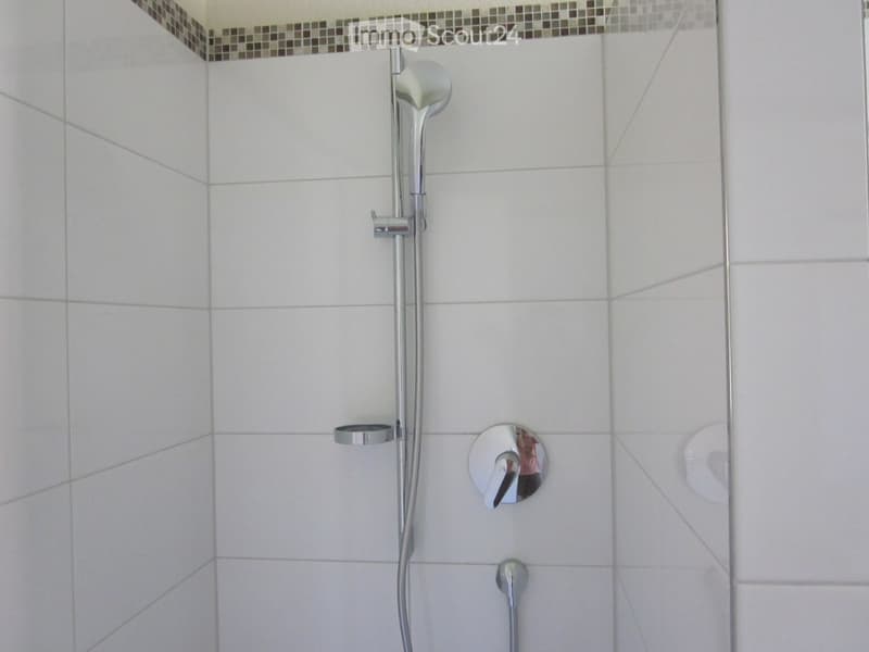 A shower cubicle with a shower head, flexible hose, and soap holder. Tiled walls and floor.