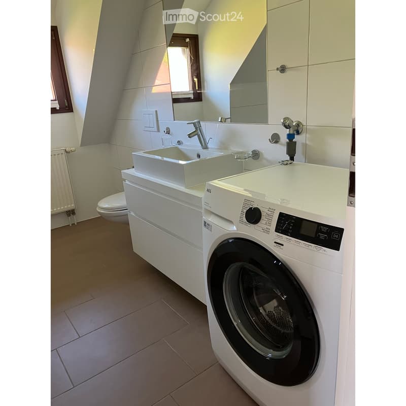 Bathroom. Modern bathroom with a white sink, mirror, and a washing machine. The space includes a toilet and a window with a curtain.