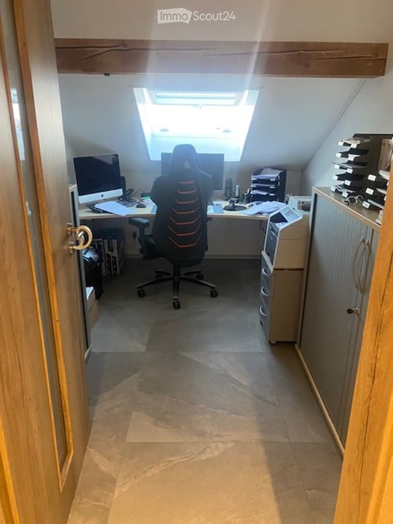 A well-lit home office with a large skylight, a modern ergonomic chair, a desk with a computer, and a printer on a cabinet.