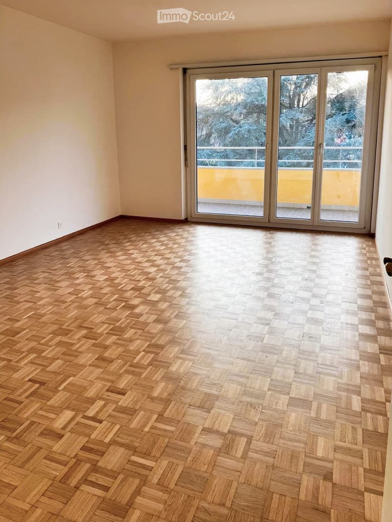Empty room with wooden herringbone flooring, white walls, and large sliding glass doors leading to a balcony.