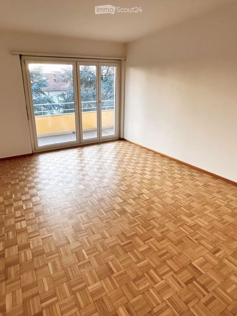 Empty room with wooden herringbone flooring and large sliding glass doors leading to a balcony.