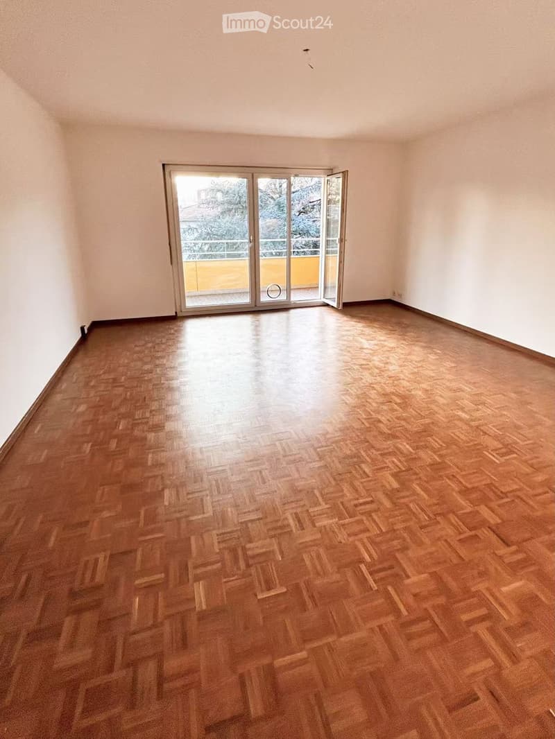 Empty room with wooden parquet flooring and large sliding glass doors leading to a balcony.