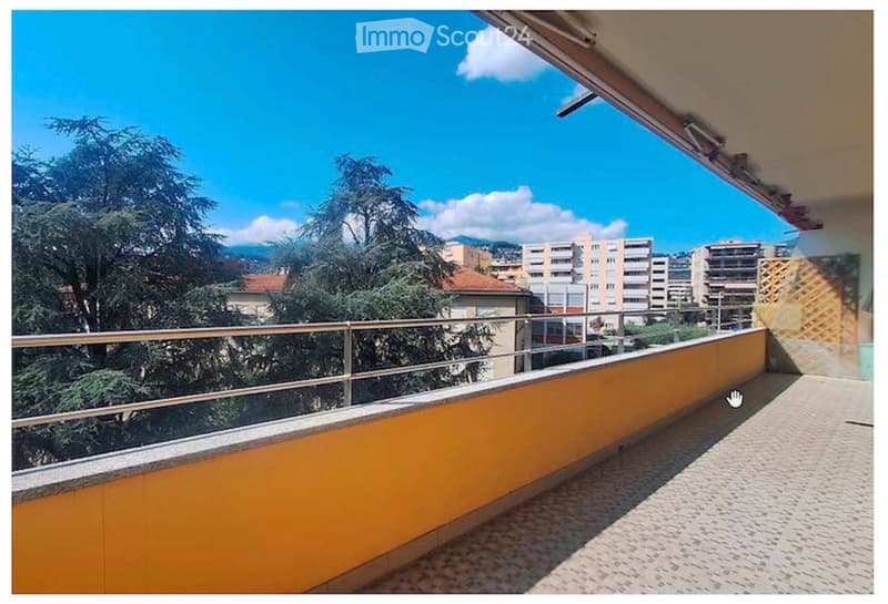 Balcony with metal railing, tiled floor, overlooking a cityscape with trees and buildings.