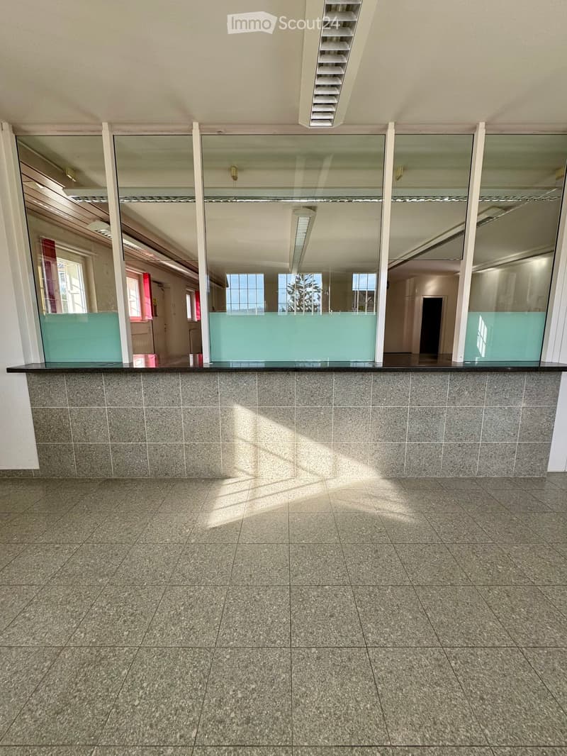 Empty hallway with tiled floor, grey walls, and a glass partition reflecting adjacent rooms.