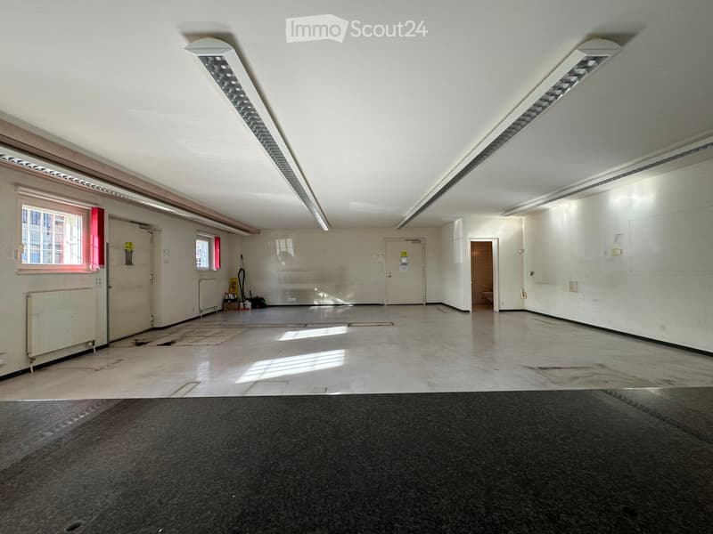 Empty room with white walls, concrete floor, fluorescent lighting, and a few windows. No furniture or equipment present.