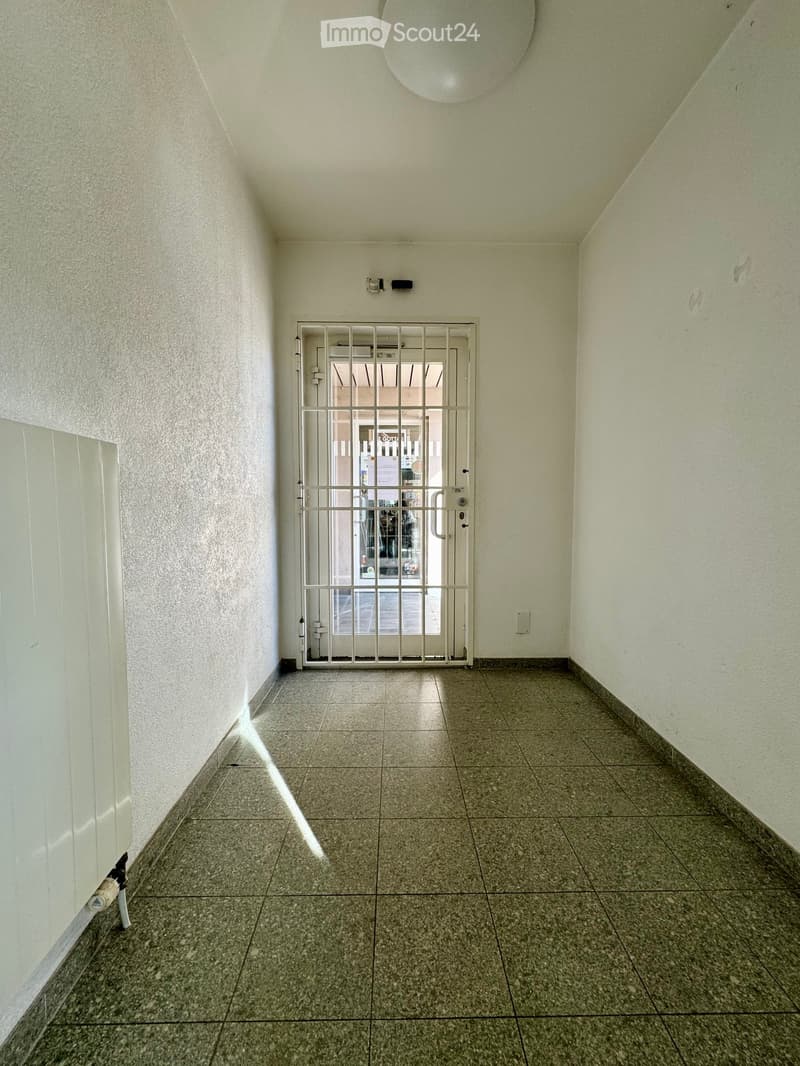 Empty hallway with tiled floor, white walls, and a metal security door at the end.