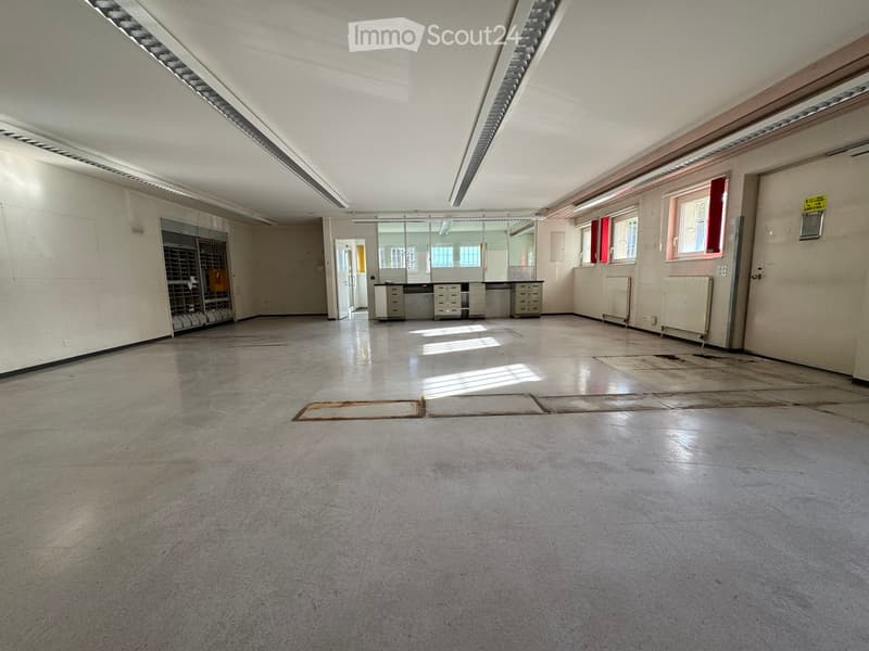 Empty room with bare walls, concrete floor, and minimal fixtures including a small cabinet and a few windows with red curtains.