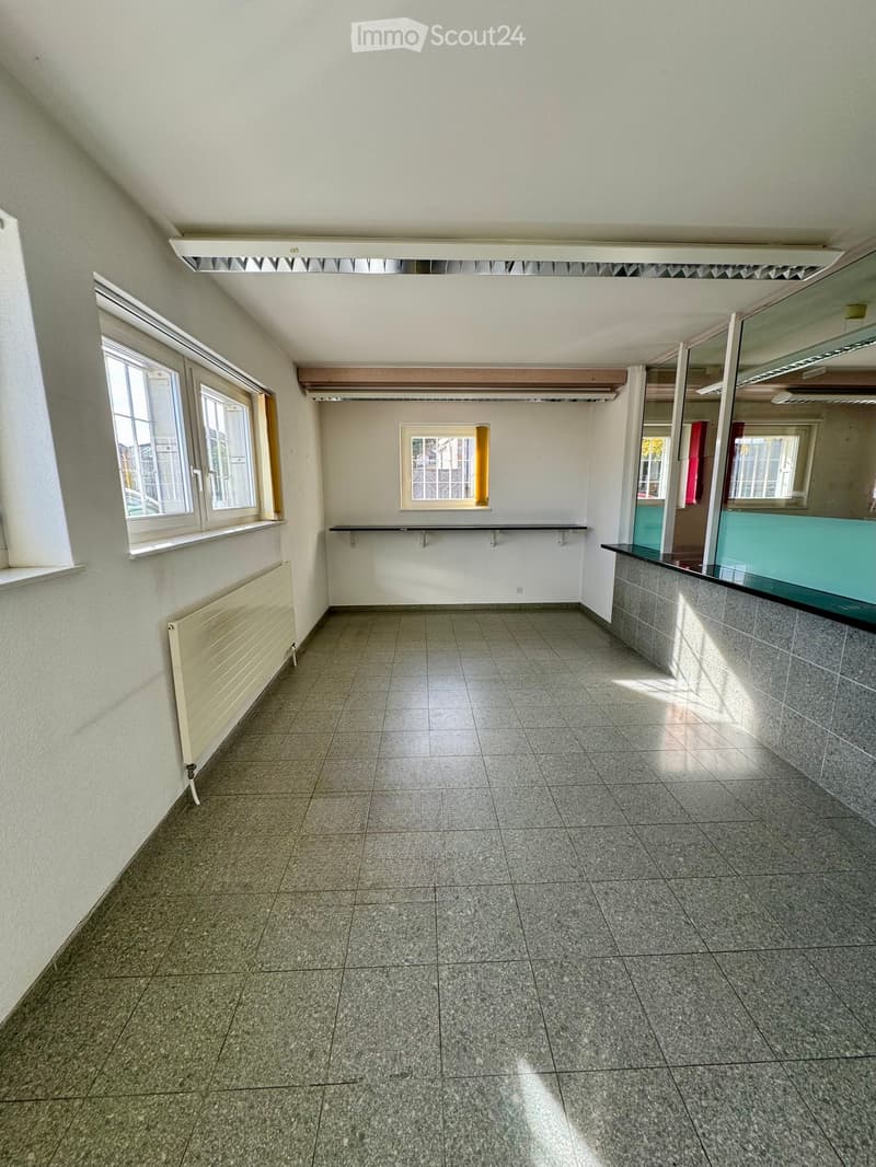Empty room with tiled floor, white walls, windows, radiator, and a small counter with a mirror.