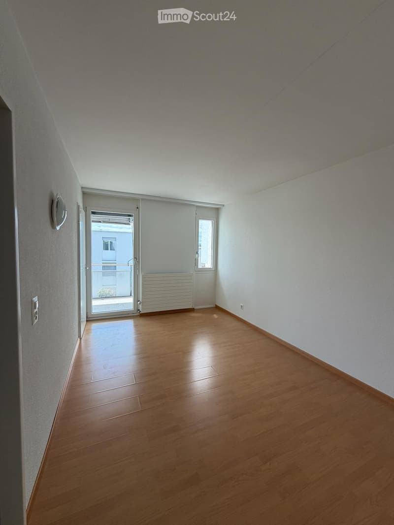 Empty room with wooden flooring, white walls, and a sliding glass door leading to a balcony.