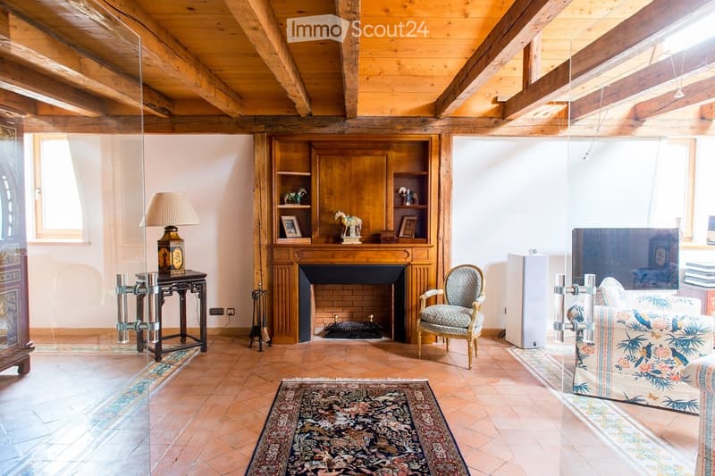 Living room with exposed wooden beams, fireplace, sofa, armchair, table with lamp, and cabinet with decorative items.