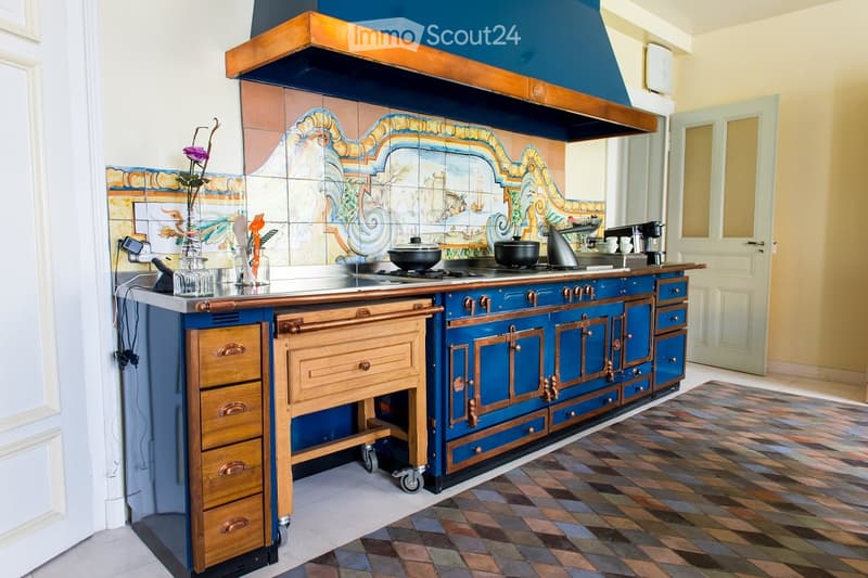 A kitchen with a blue and wooden stove, cabinets, a coffee maker, and a decorative tile backsplash.