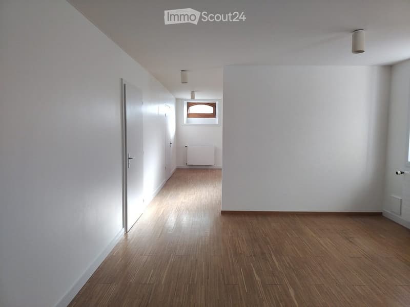 Empty hallway with wooden flooring, white walls, and a single window at the end.