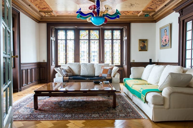 Elegant living room with wooden floors, large stained-glass windows, a colorful chandelier, two sofas, a coffee table, and framed artwork on the walls.