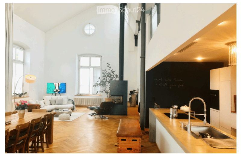 Open-plan living and dining area with a modern fireplace, white walls, large windows, and a kitchen area with a counter and sink.