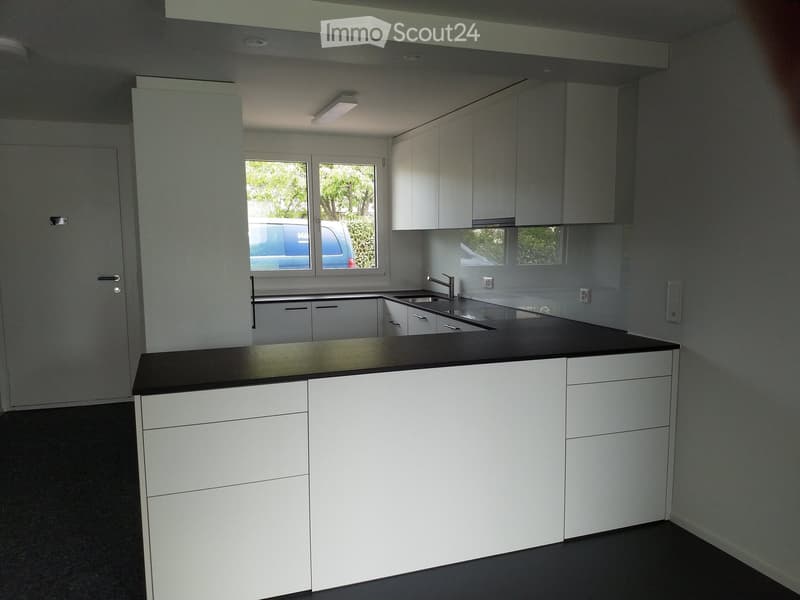 modern white kitchen with island, black countertops, stainless steel sink, gas stove, dishwasher, refrigerator