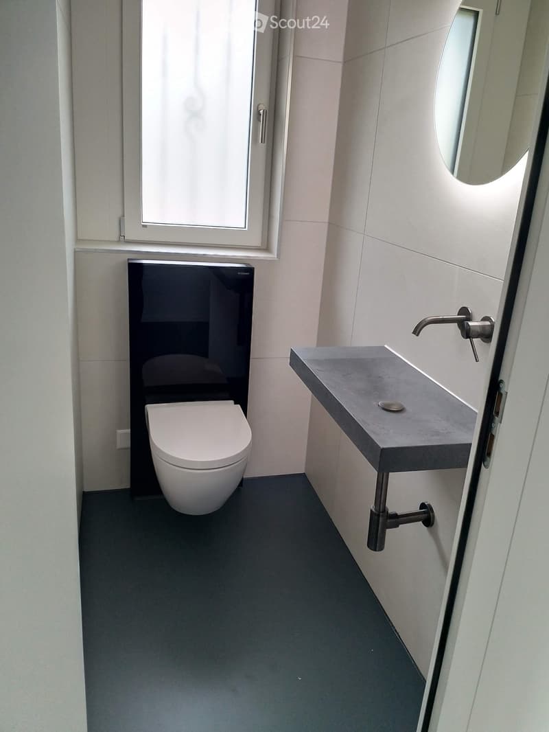 Modern minimalist bathroom with white toilet, grey countertop, round mirror, and stainless steel faucet