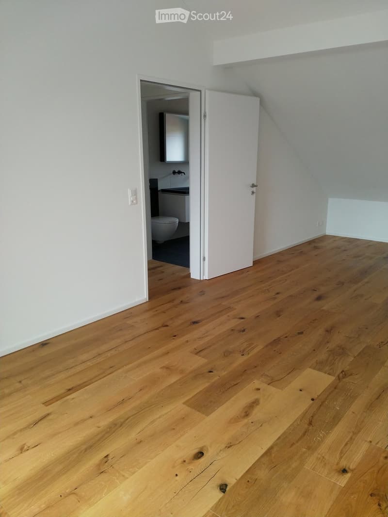 Open attic room with wooden floor, white walls, bathroom in the corner.