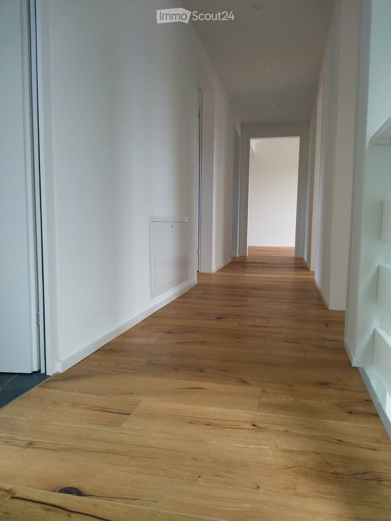long hallway with wooden flooring, white walls, closed doors, clean and empty