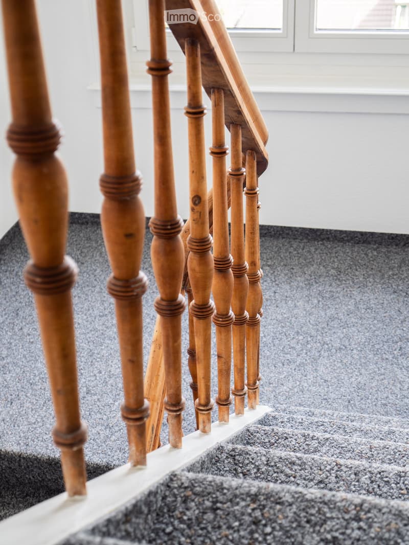 Close-up view of a wooden staircase with turned balusters and a carpeted stair tread, leading upwards.
