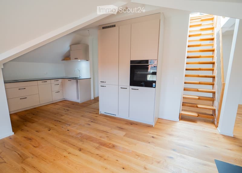 Modern kitchen with light-colored cabinets, wooden flooring, and a small staircase leading upwards.