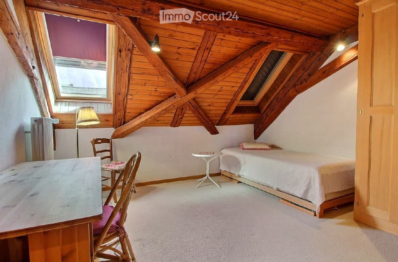 Cozy attic bedroom with wooden beams, skylight windows, a single bed, a small table, and chairs.