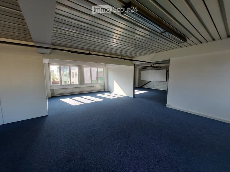 Empty room with blue carpet, white walls, large windows, and exposed ceiling beams.
