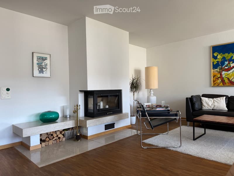 Modern living room with a fireplace, a black leather sofa, a wooden coffee table, a white floor lamp, and a decorative vase on a marble shelf.