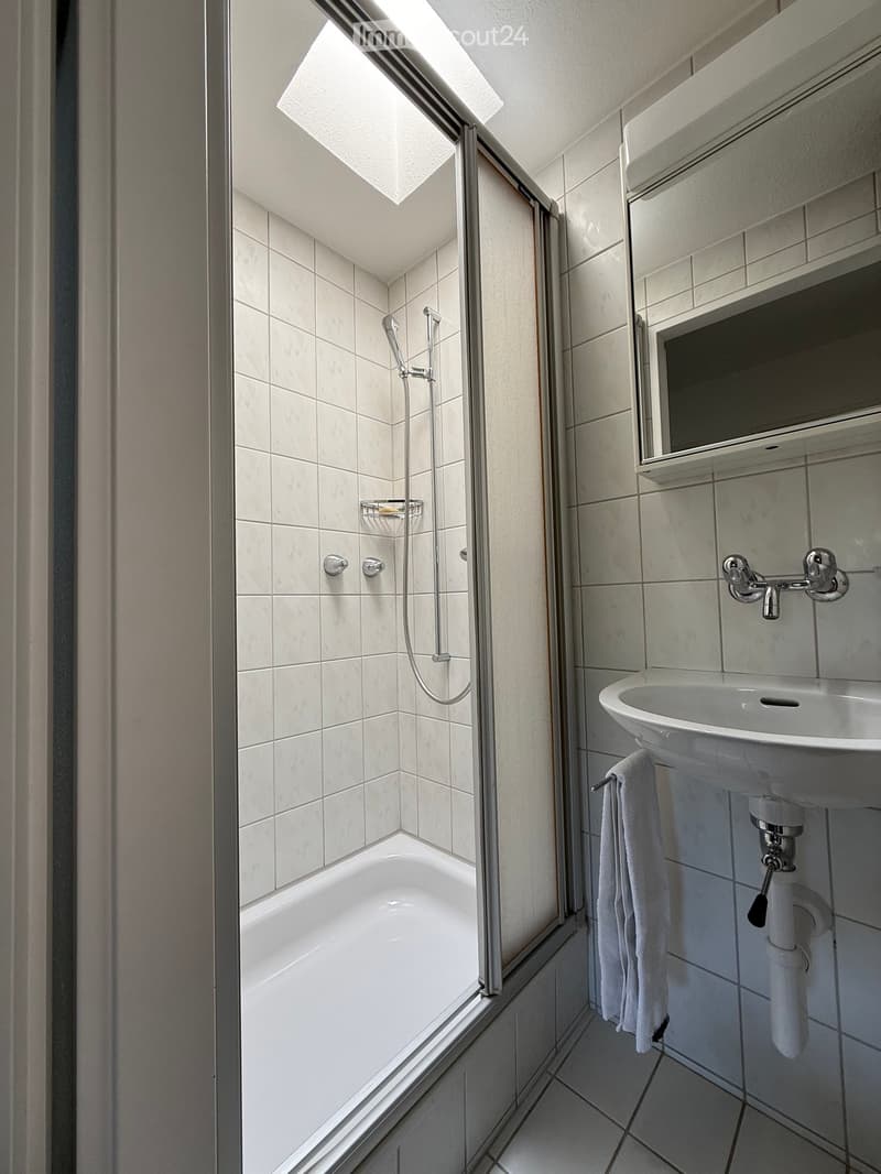 Modern bathroom with a bathtub, glass shower enclosure, sink, mirror, and towel.