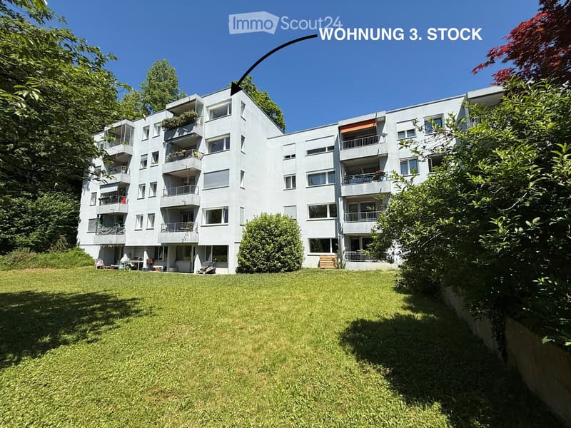 Modern multi-story apartment building with balconies, surrounded by greenery and a well-maintained lawn.