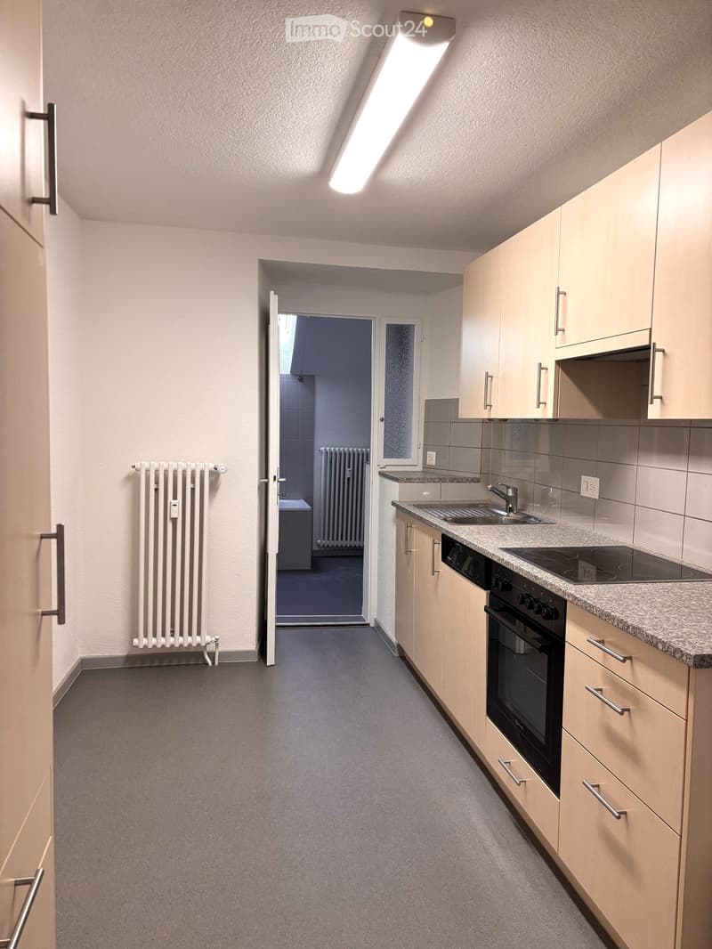empty kitchen with gray floor, white walls, wooden cabinets, granite countertop, sink with faucet, electric stove, dishwasher, radiator, ceiling lamp