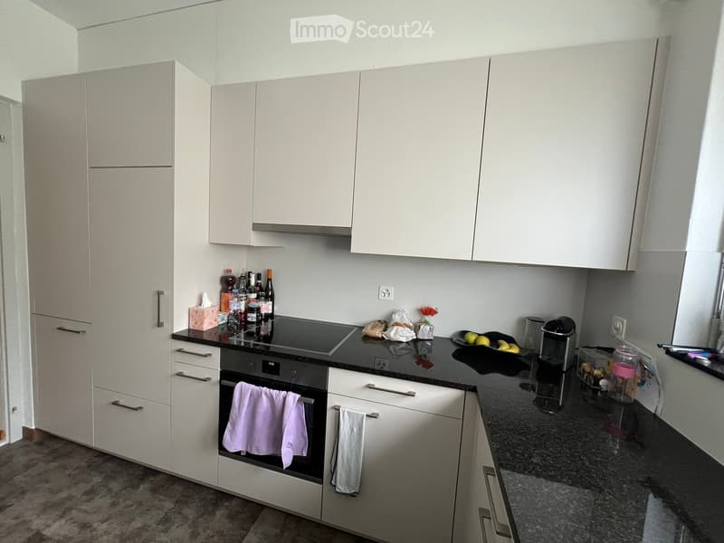 Modern kitchen with white cabinets, black countertops, and stainless steel appliances. Includes an oven, coffee maker, and various kitchen items on the counter.