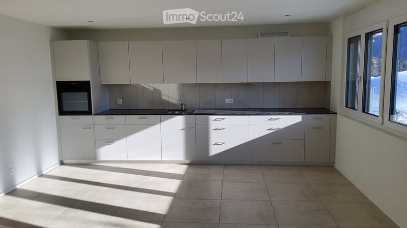Modern kitchen with white cabinets, a sink, and an oven, featuring tiled flooring and large windows letting in natural light.