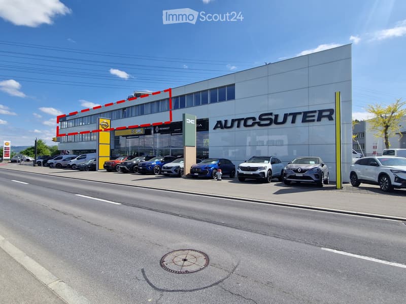 Modern car dealership building with large glass windows and signage for 'AUTOSUTER', several cars parked in front.