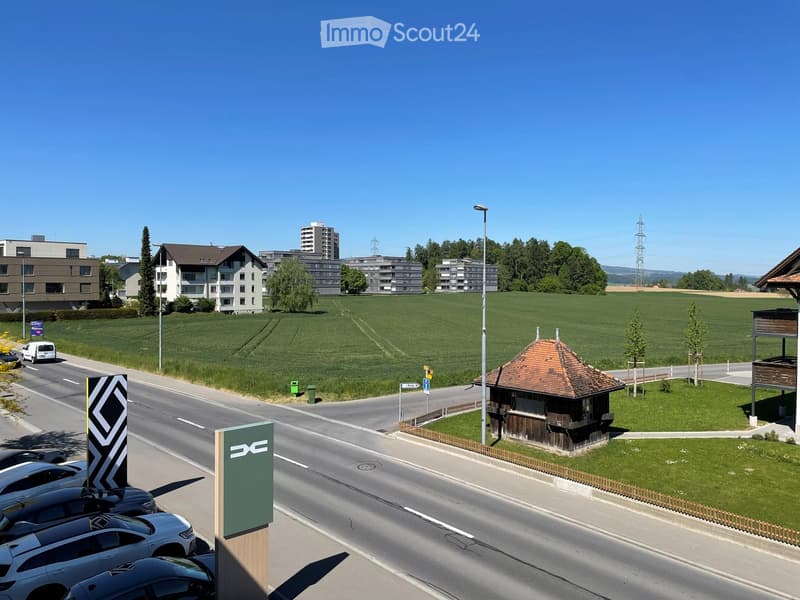 Residential area with multi-story apartment buildings, a small wooden gazebo, a parking lot, and a green field.