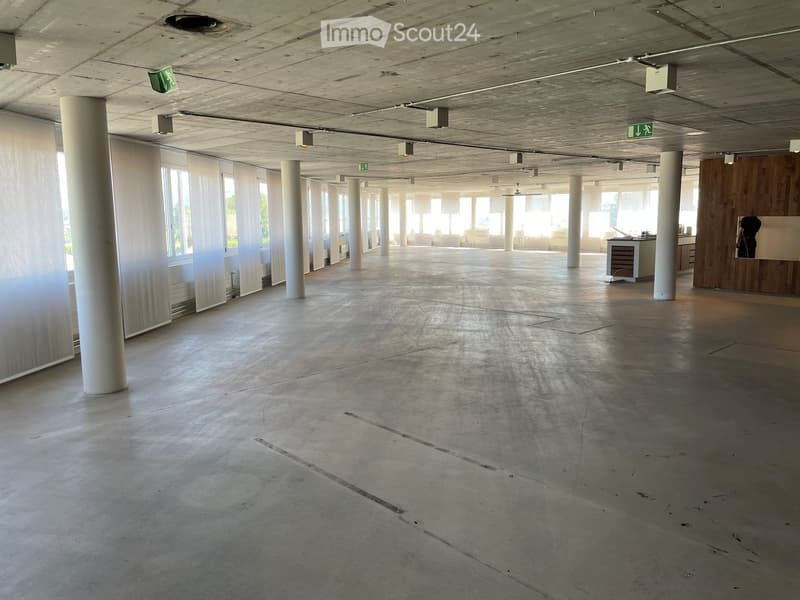Empty room with concrete floor, large windows with white blinds, white pillars, and a small counter area with cabinets and a sink.